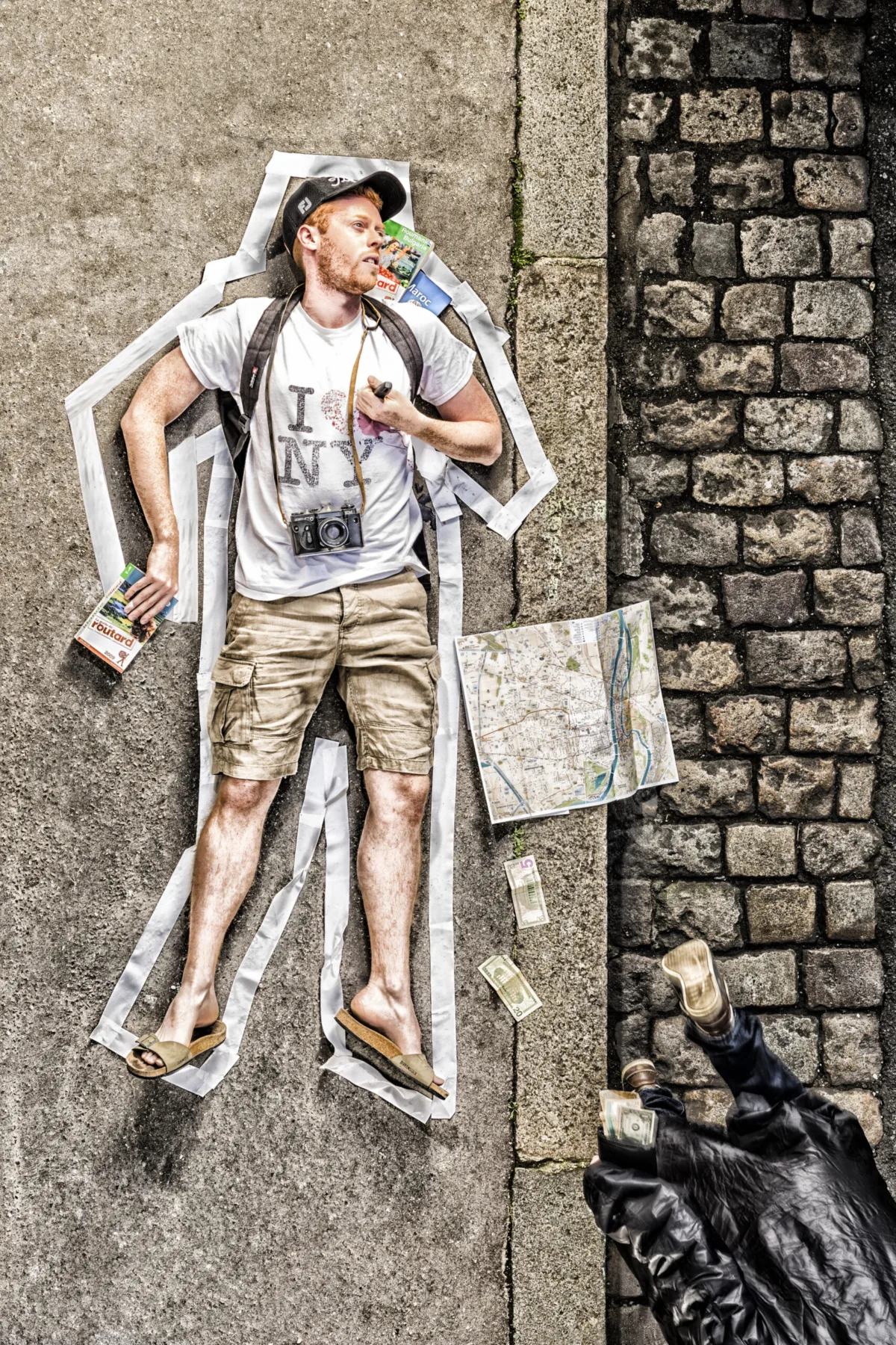 A tourist lies on cobblestones inside a chalk outline, map and camera beside him