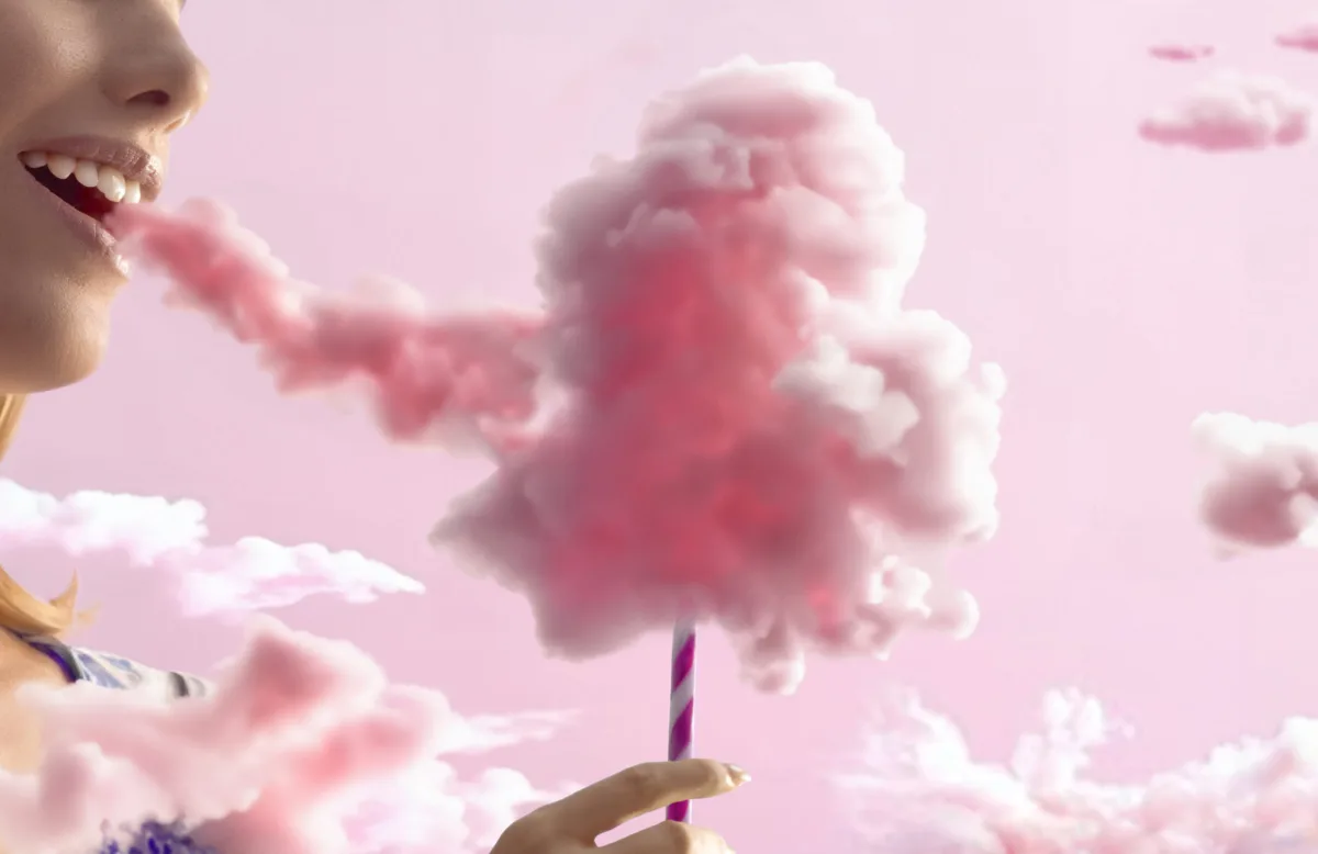 A smiling woman eats a pink cloud like candy floss