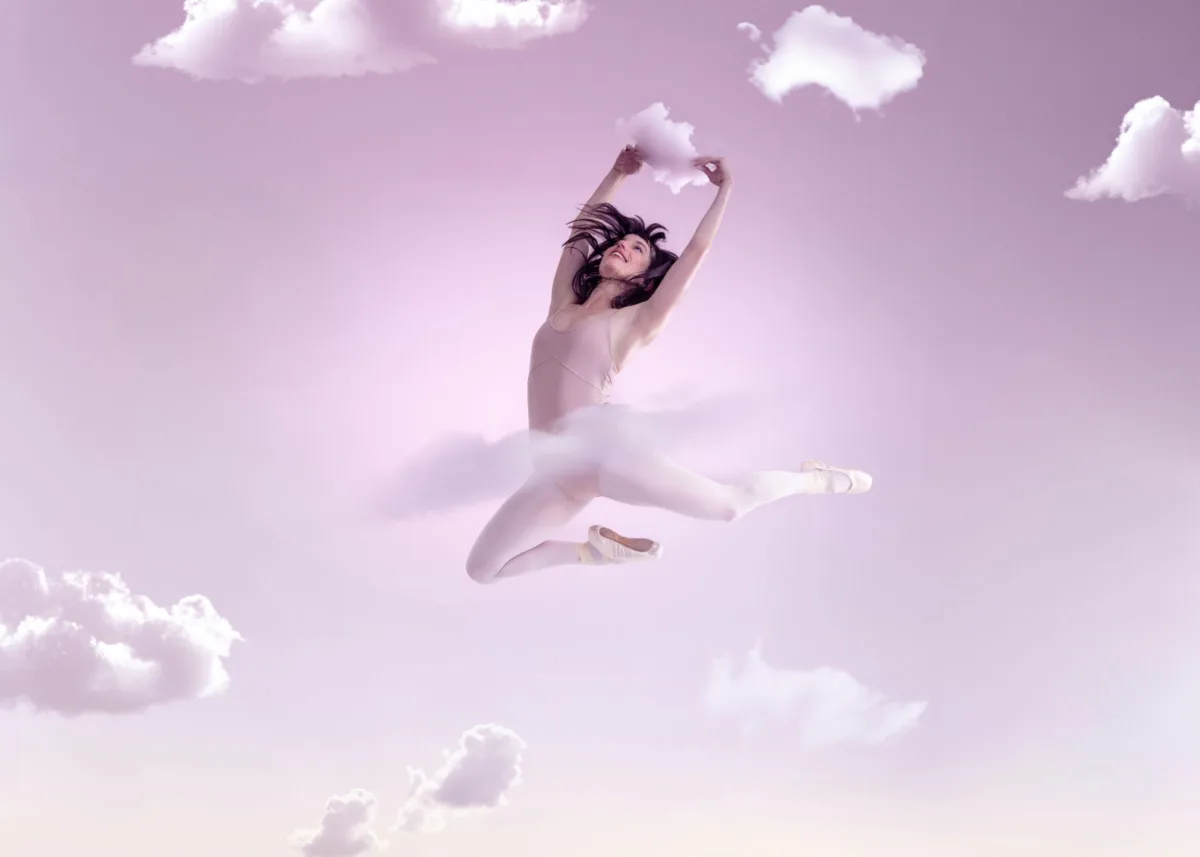 A dancer leaps among small clouds in a pink sky