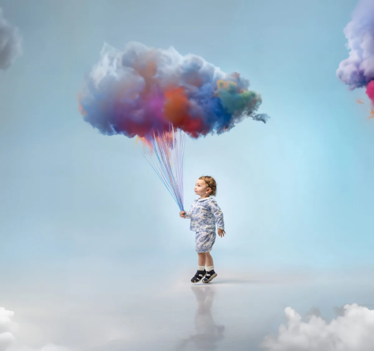 A small child holds a bunch of rainbow clouds like balloons
