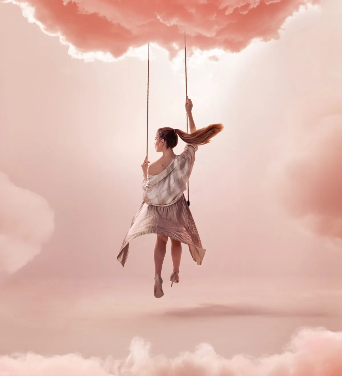 A woman on a swing hanging from a pink cloud