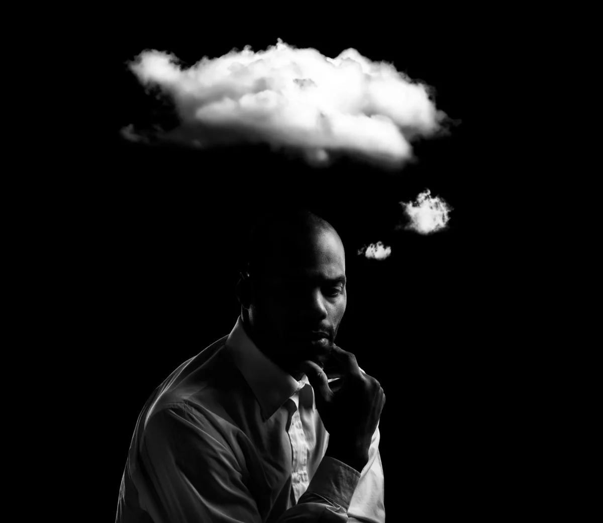 A man lost in thought beneath his own cloud, on black
