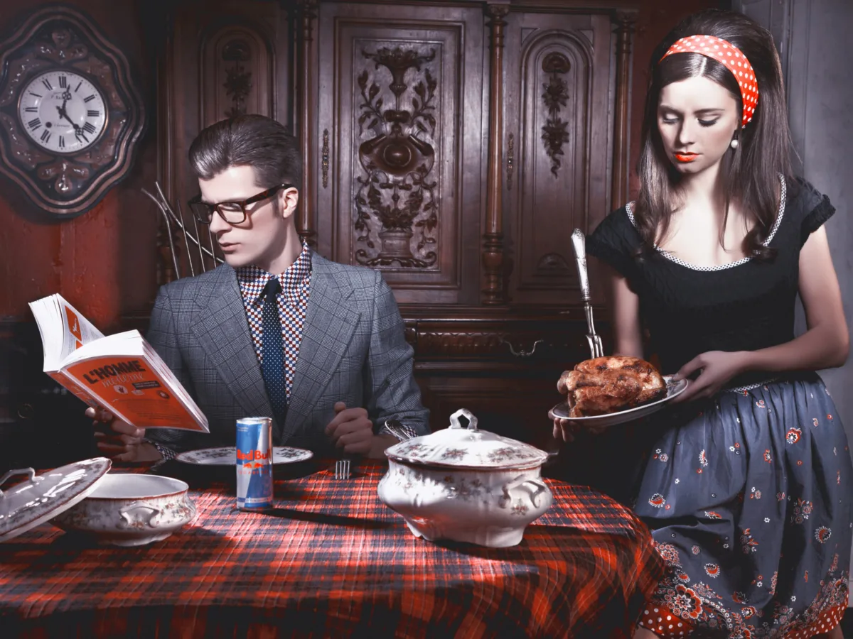 Staged interior: a couple at a checked-cloth dinner table, he reads, she serves