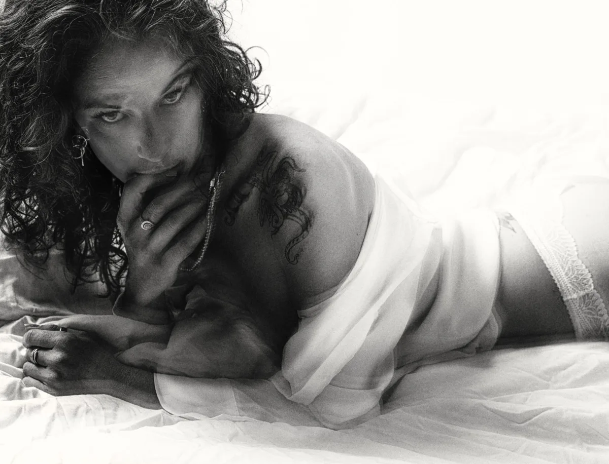 Black-and-white: a woman lies on white sheets, her face turned toward the light