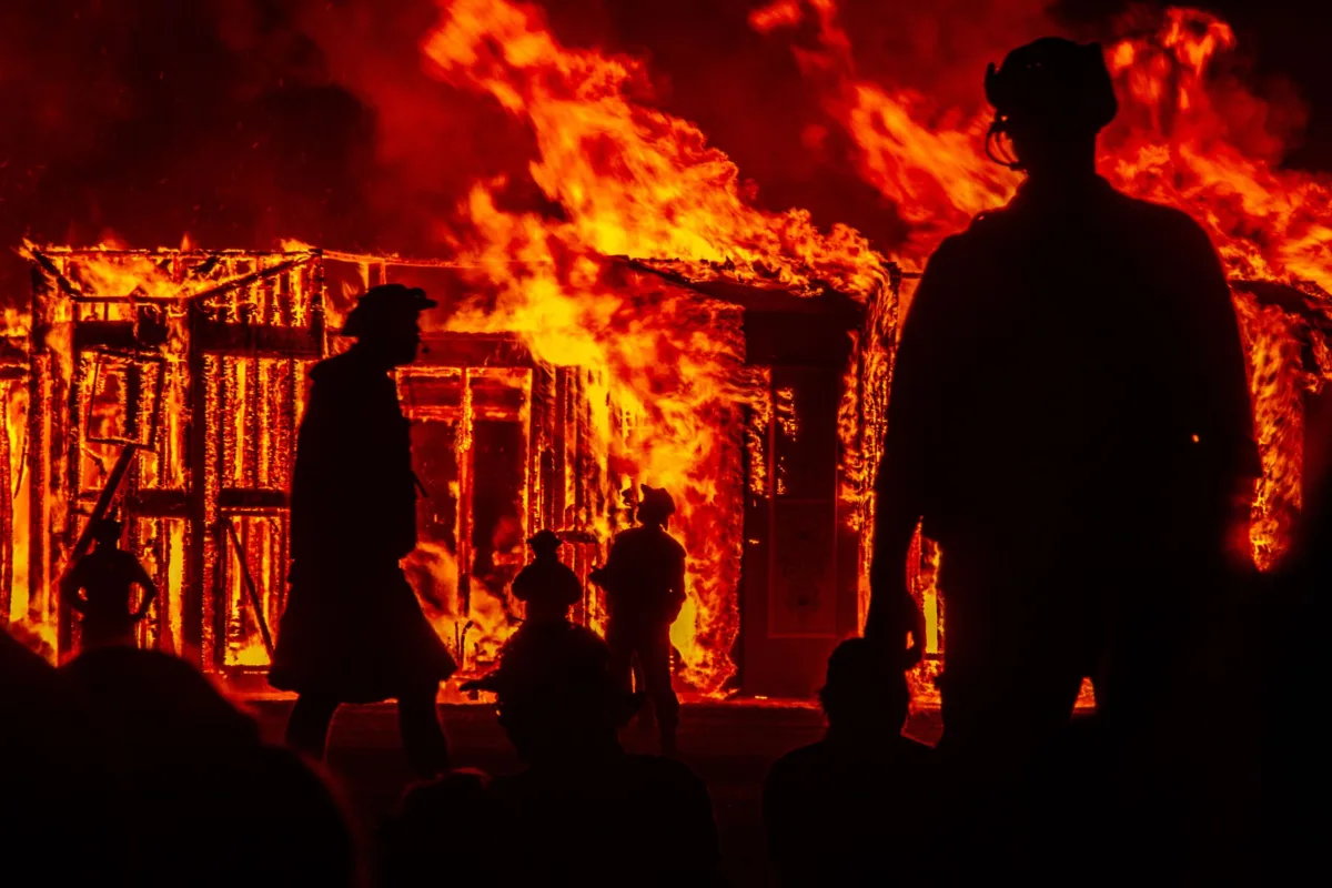 Silhouettes watch a wooden structure burn at night