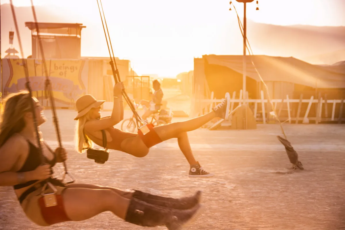 Figures on a swing silhouetted against a desert sunset